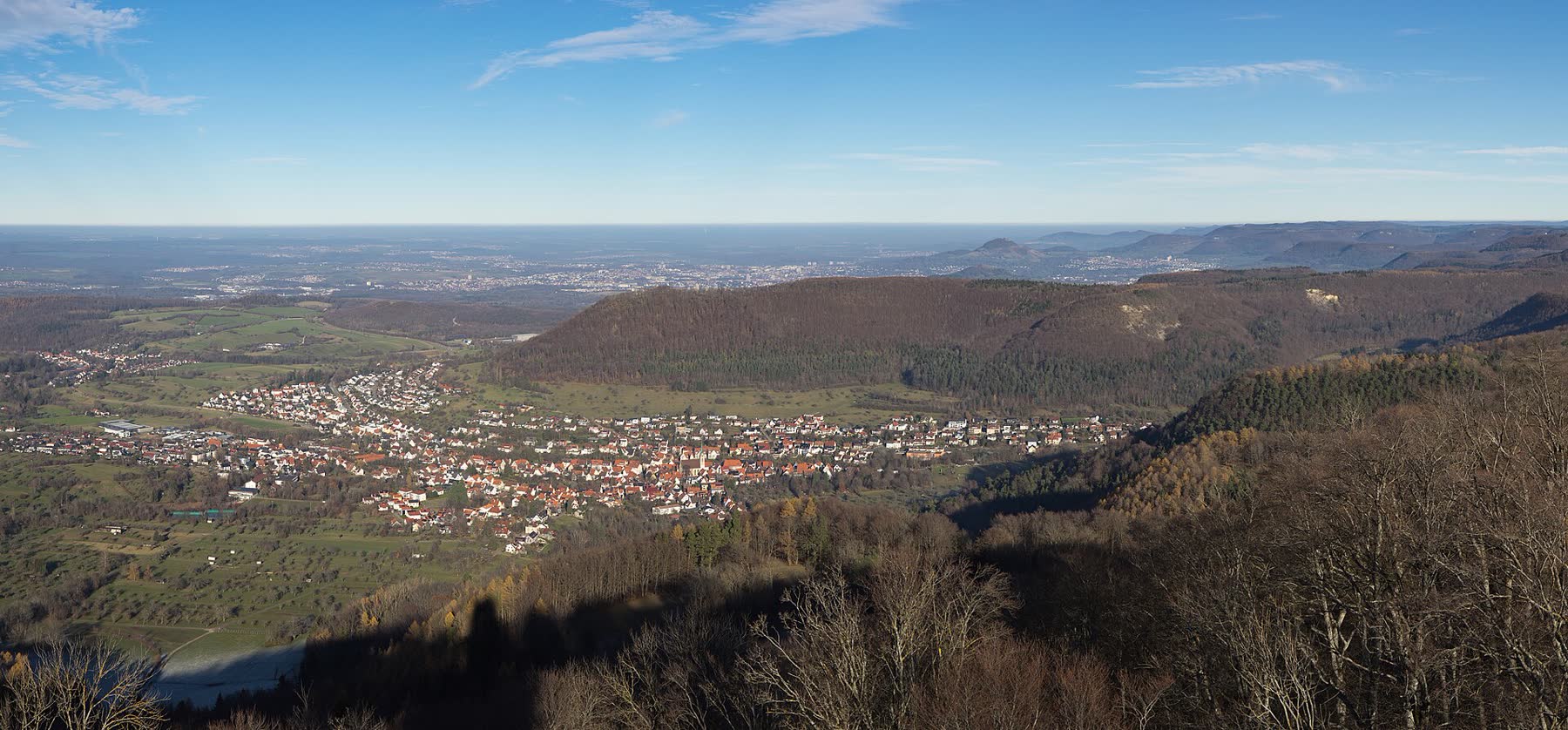 Blick über ein Dorf und den bewaldeten Albtrauf der Schwäbischen Alb